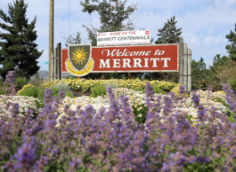 A sign reading Welcome to Merritt surrounded by yellow, white and purple flowers.