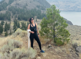 A woman wearing outdoor gear poses for a picture high up in a forested area overlooking water