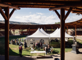 People gather in the middle of a circular wooden enclosure where white tents are set up.