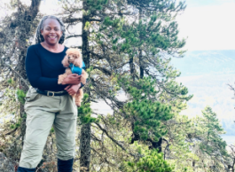 A woman with a dog in her hands poses for a photo in front of a large tree.