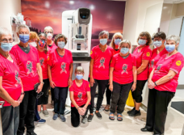 A group of people wearing pink shirts and masks pose for a picture inside.