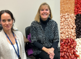 Two women sitting on chairs, one with dark hair in a pony tail and wearing a beige sweater and lanyard, the other with medium-length blonde hair wearing a black and white blouse. To the right is a photo of six kinds of dried beans