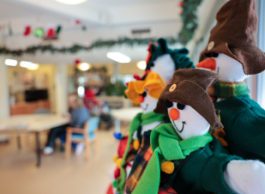 Three stuffed snowpeople in brown hats and green shirts on display with a blurred background of tables, chairs and people