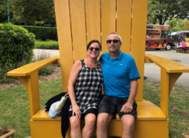 A man and woman wearing sunglasses and summery clothes sitting on a large yellow chair outside.