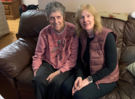 Two women, one with short grey hair and one with medium long blonde hair, sit together on a brown leather couch