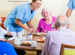 A healthcare worker and seniors gathered together around a table for coffee