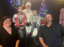 Two adults and two young children pose with Santa with a Christmas tree in the background