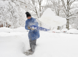 A person wearing outdoor gear shovels snow.