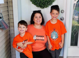 A woman and two boys pose for a picture in matching orange t-shirts