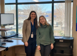 Two young women in business attire stand together in a sunny office