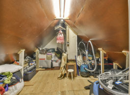 An attic with a triangular roof full of clothes, bins, a vacuum and a stool