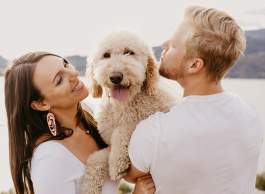 A man holding a dog with his back to the camera and a woman on the other side of the dog holding the two of them smiling.