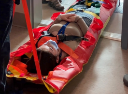 An individual is secured on a stretcher with bright red and yellow colors, receiving medical assistance in an indoor setting.