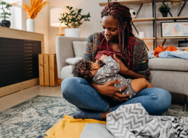 A mother sits on the floor and breastfeeds her infant