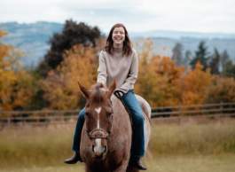 Woman in beige sweater and jeans riding a horse in the fall