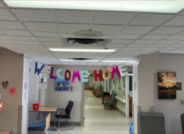 Interior of a room decorated with "WELCOME HOME" banners, balloons, and paintings on the walls, including chairs and tables set up for visitors.