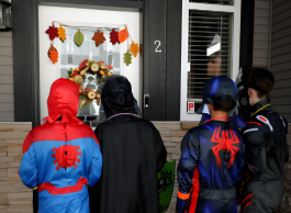 four kids in hero costumes trick-or-treating at a house