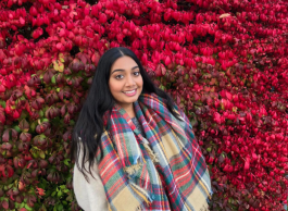 A smiling woman stands in front of a wall of flowers for a picture