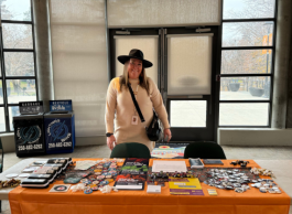 A person standing behind a promotional table filled with informational brochures and badges inside a building.